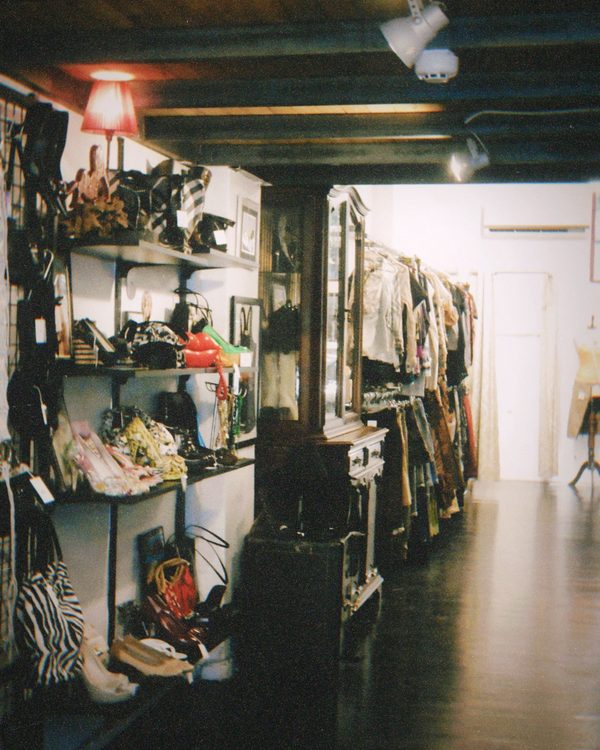 A long narrow shop interior with shelves of bags and shoes on one side and a rail of clothes running to the back