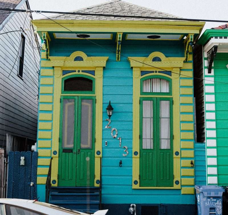 A narrow shotgun house storefront in New Orleans with tall double doors under carved brackets