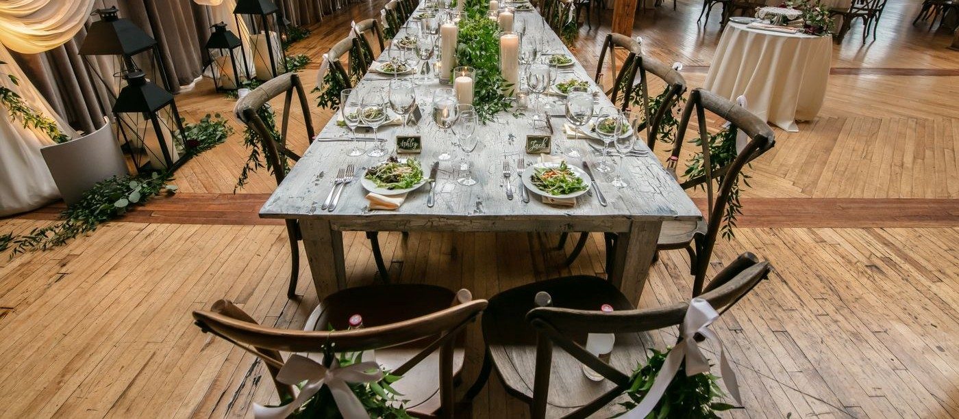 A long wooden table set for dinner with candles, greenery and place settings down its length