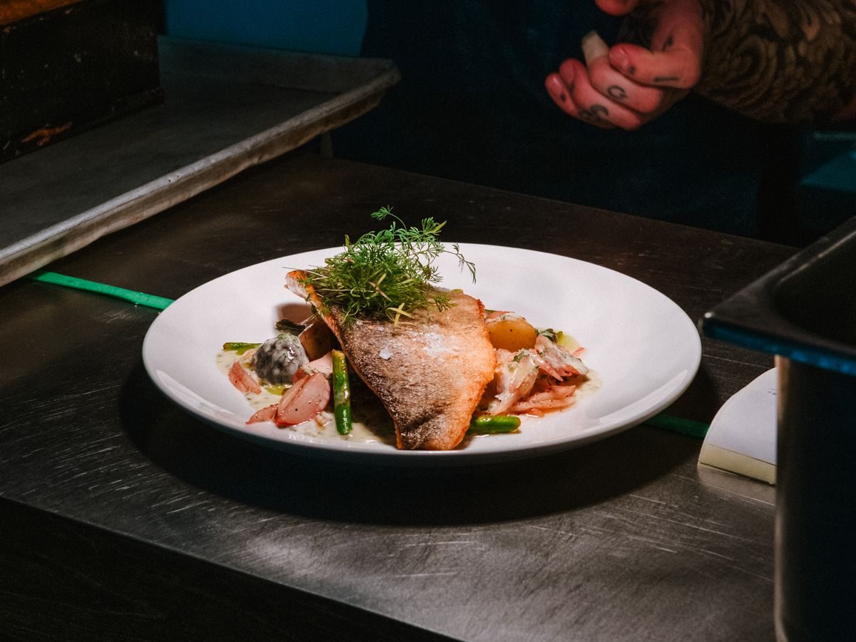 A crisp skinned fillet of fish plated with potatoes, greens and herbs