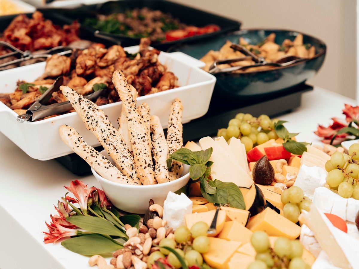 A catering spread of cheeses, grapes, breadsticks, nuts and warm dishes laid along a table