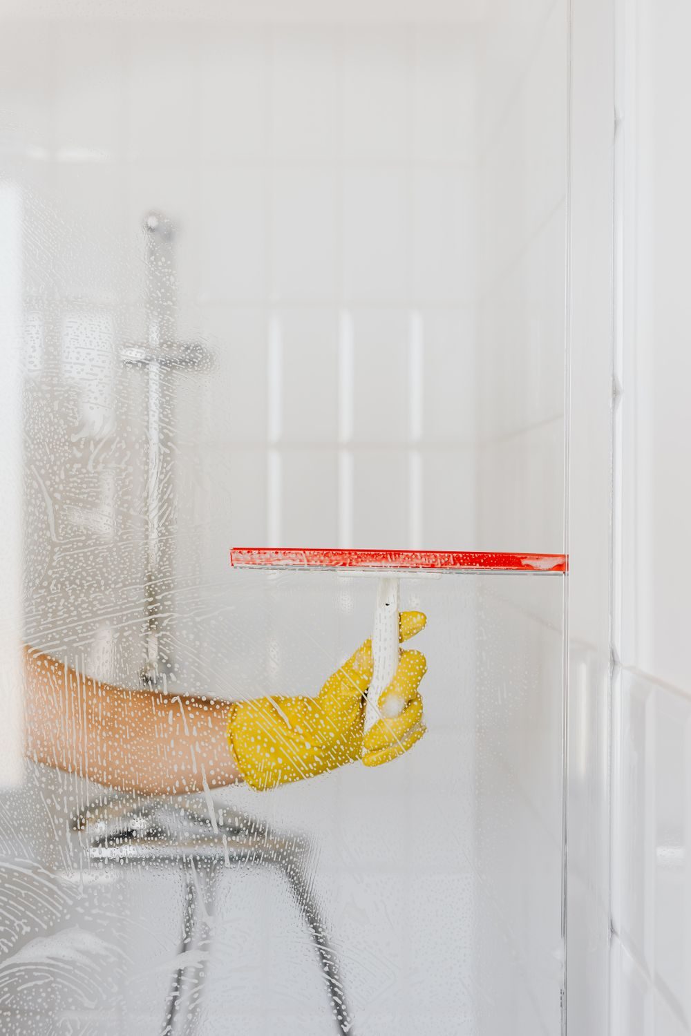 A gloved hand drawing a squeegee down a wet glass shower screen