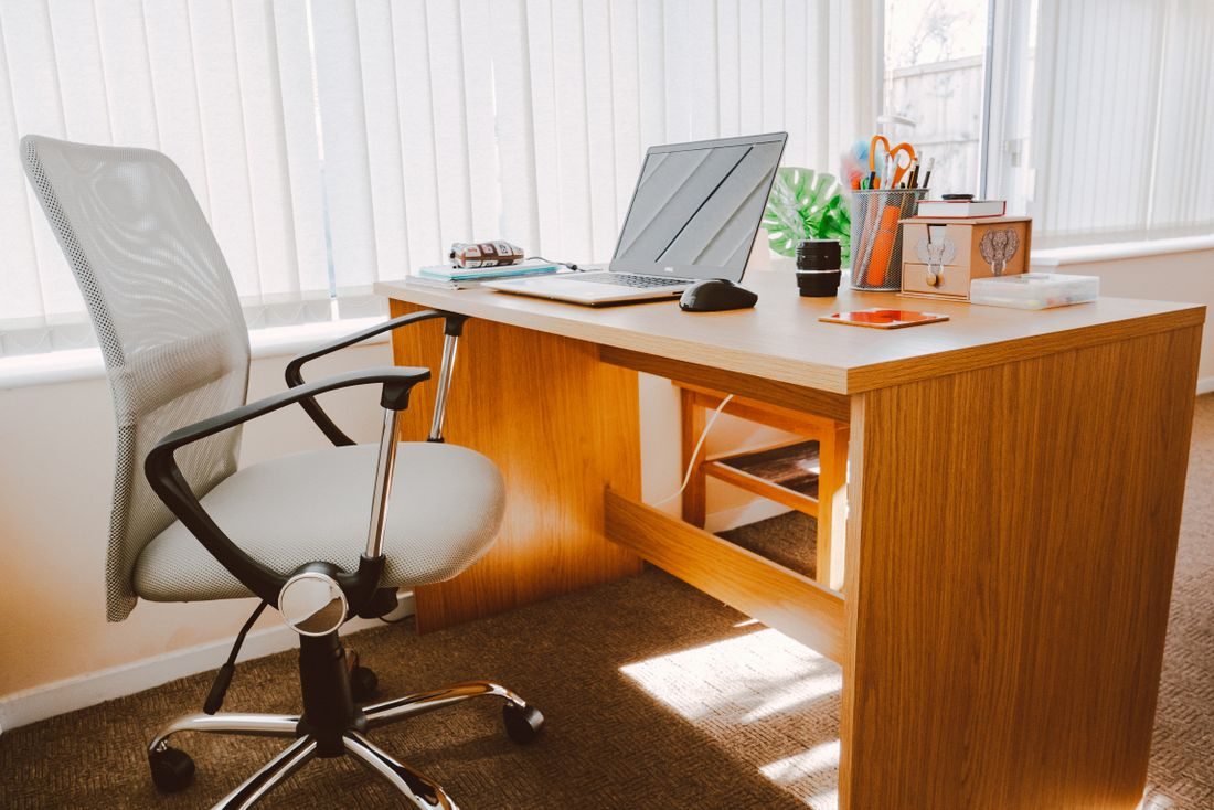 A tidy office desk and chair beside a sunlit window