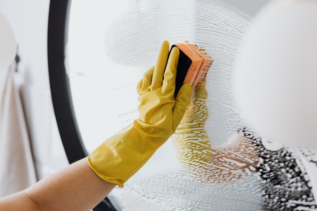 A gloved hand wiping a soapy bathroom mirror clean