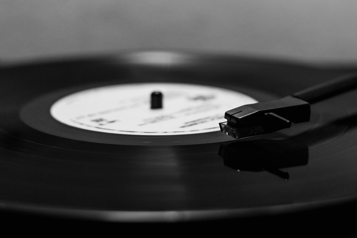 Black and white close up of a tonearm resting on a spinning record with a plain white label