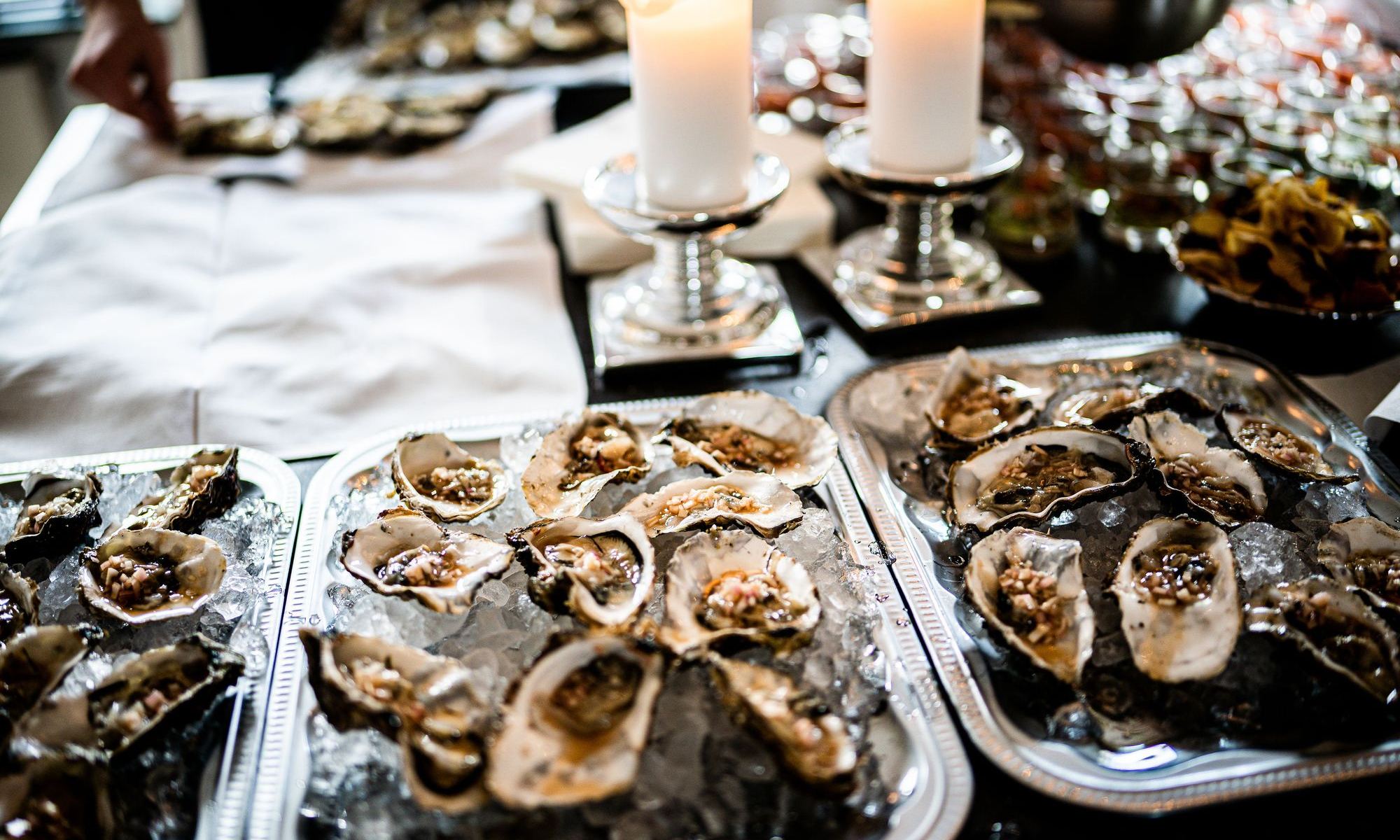 Trays of raw oysters on crushed ice, dressed with mignonette, beside two pillar candles in silver holders