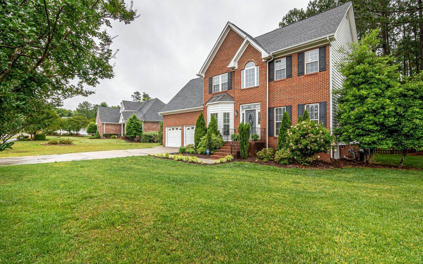 A brick house with a wide mown front lawn and planted beds