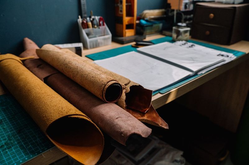 Rolled sides of tan and brown vegetable tanned leather on a workbench beside a binder of paper patterns