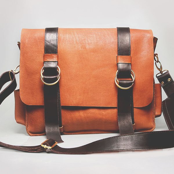 A cognac messenger bag with chestnut straps and brass rings
