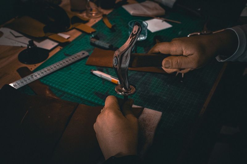 Hands setting a rivet with a hand press on a green workbench