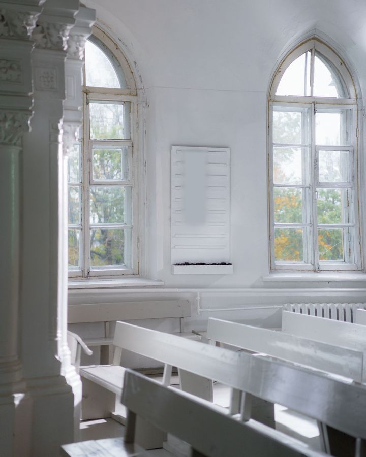 A bright white church interior with arched windows and rows of painted wooden pews