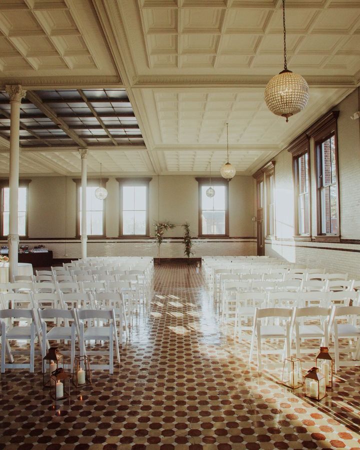 A tall event hall with rows of white folding chairs, globe pendant lights and a patterned tile floor
