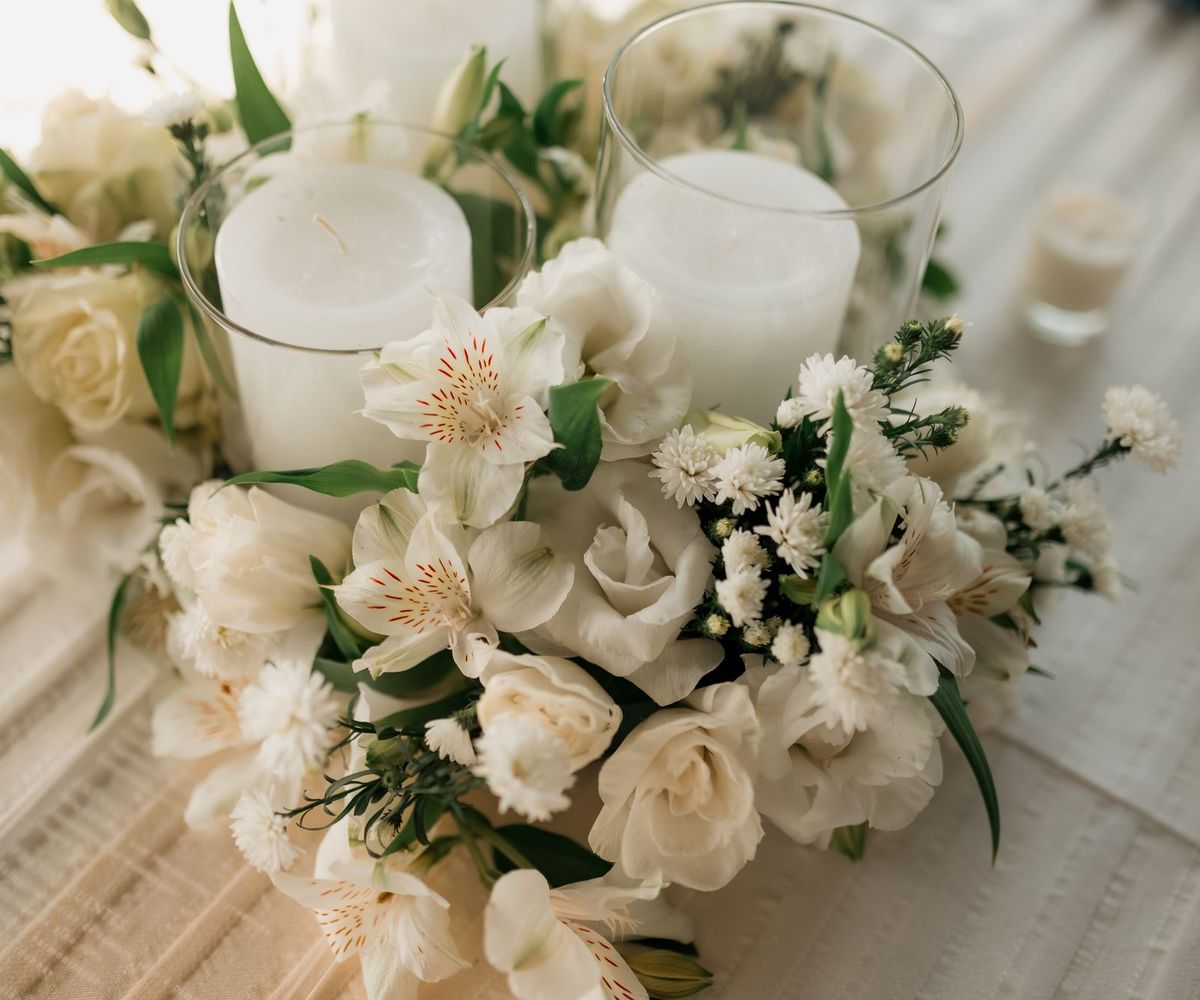 White roses, lilies and small daisies around two pillar candles in glass holders on a softly striped table runner