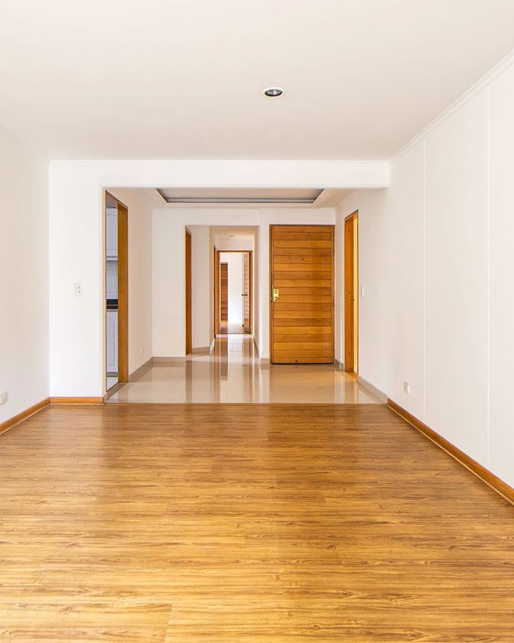 An empty, freshly cleaned apartment with white walls and warm wood floors leading to the front door