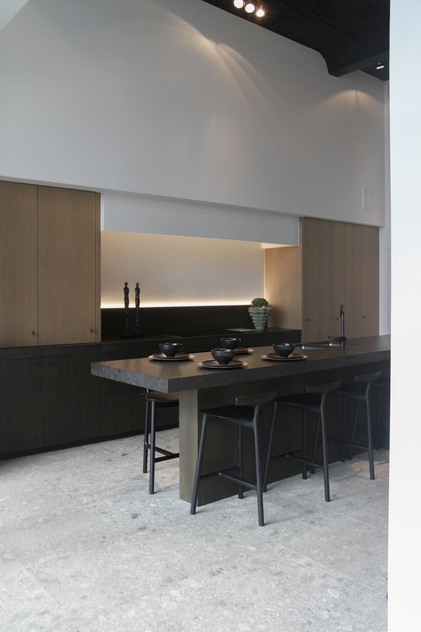 A dark, quiet interior with a long stone island, low lighting and a wall of full height glazing beyond.