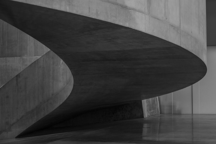 A dark curved concrete shell sweeping across a pale polished floor in an empty auditorium foyer.