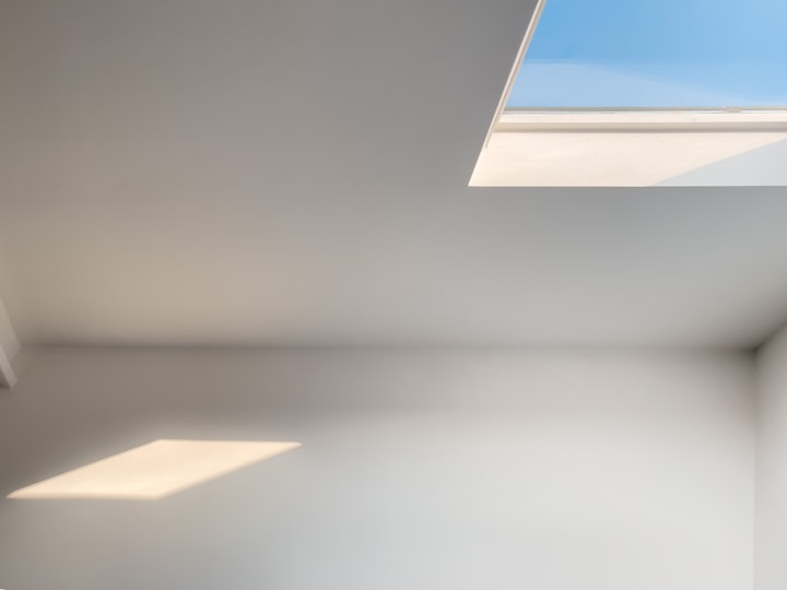 A bare white room lit by a single square skylight, which drops a bright panel of sun onto the floor.