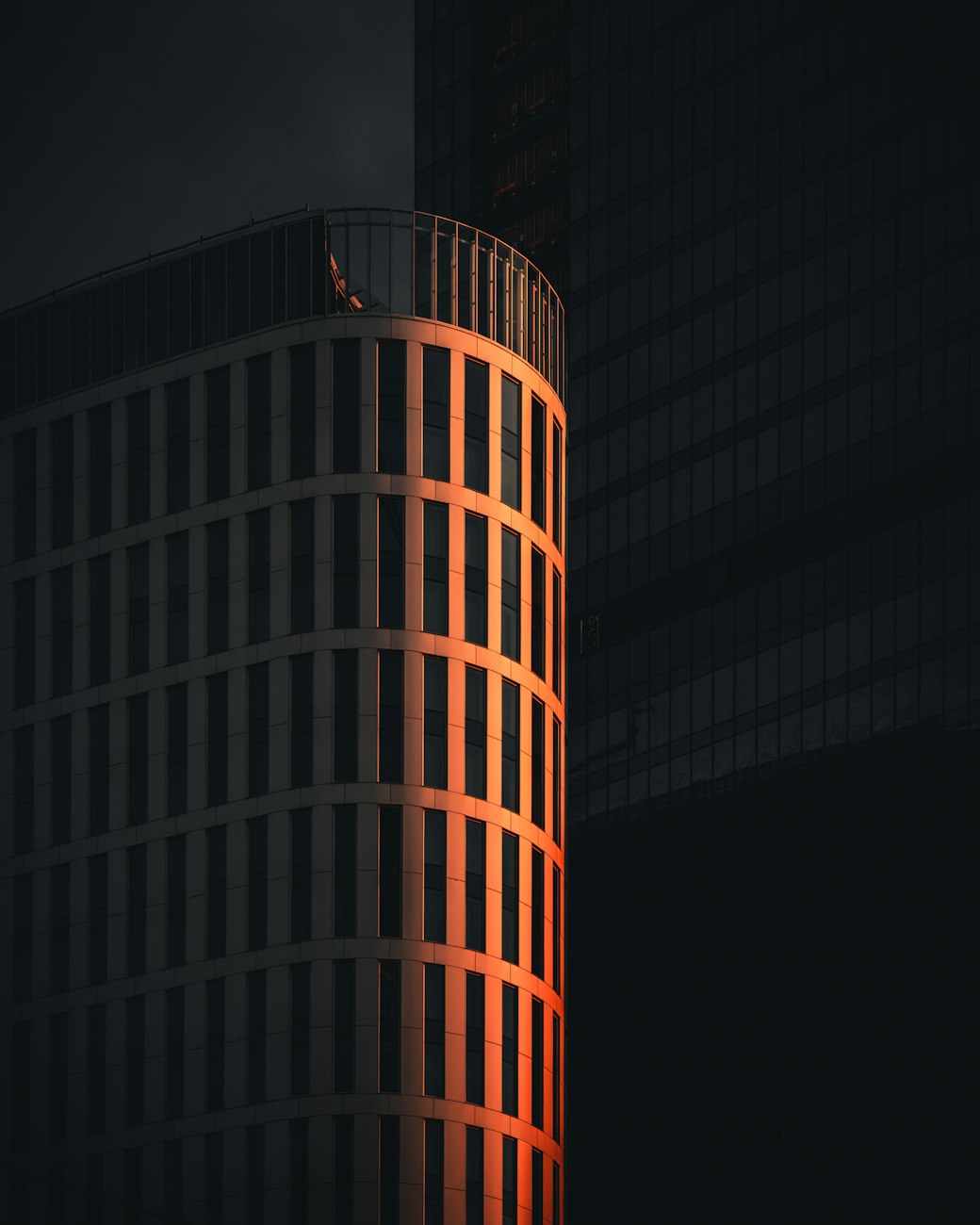 A dark cylindrical tower at dusk, its vertical fins lit from within by a band of deep orange light.
