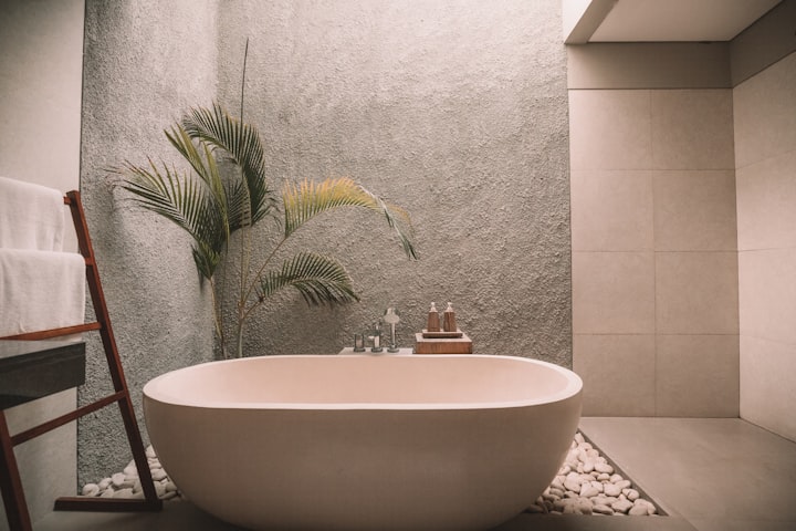 A freestanding oval bath against a warm plaster wall, with a fan palm and a timber stool alongside.