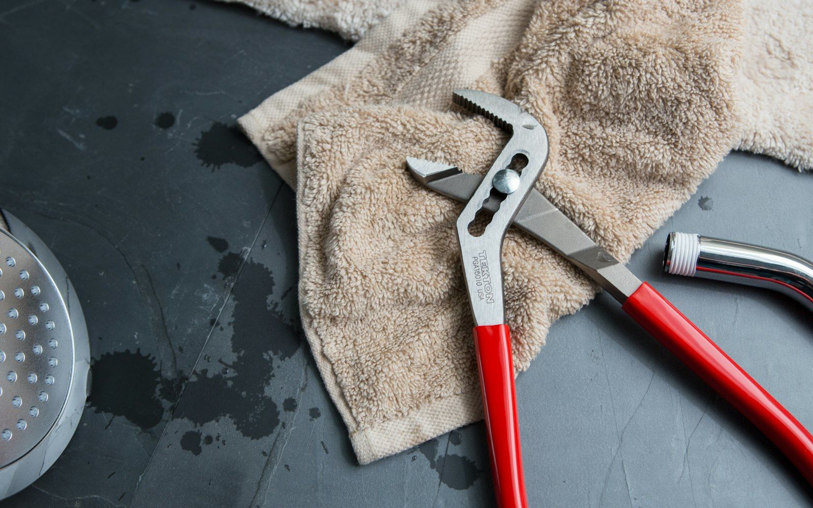 Water pump pliers resting on a towel beside a detached shower hose on a wet tiled bathroom floor