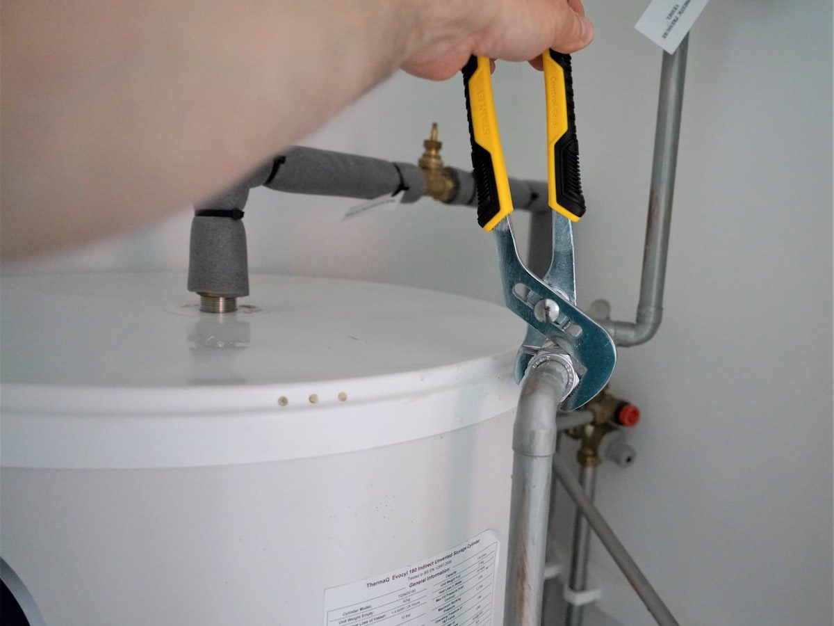 A plumber tightening a fitting on the top of a water heater with a pair of channel lock pliers