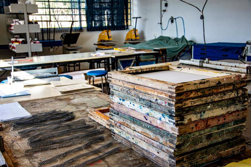 A tall stack of paint spattered wooden screen frames on a workbench in a busy print workshop