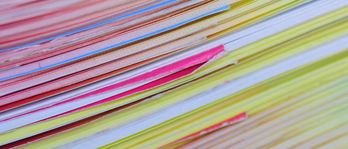 The edges of a deep stack of printing paper in pink, blue, yellow and white, fanned slightly so each sheet shows