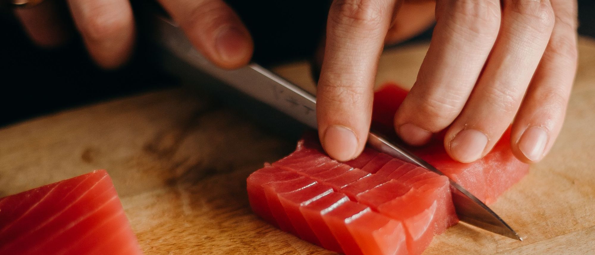 Close view of hands cutting a block of tuna into thick slices on a wooden board