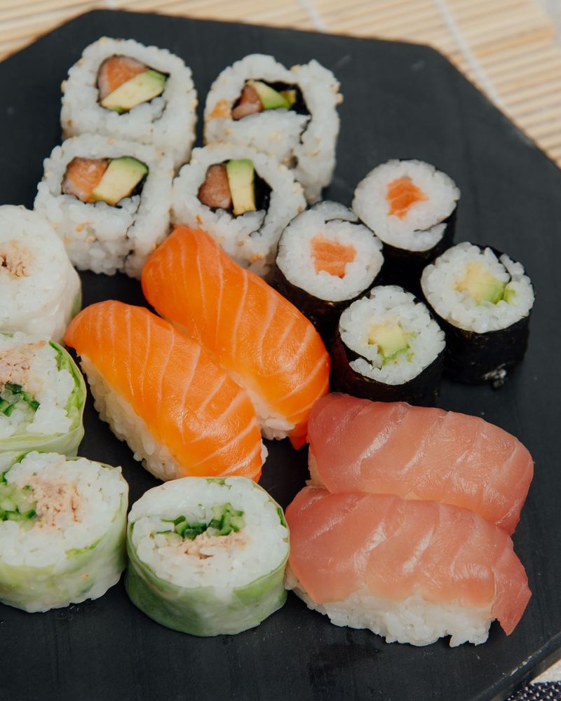 A black octagonal board of salmon and tuna nigiri, maki and cucumber wrapped rolls, packed for the table