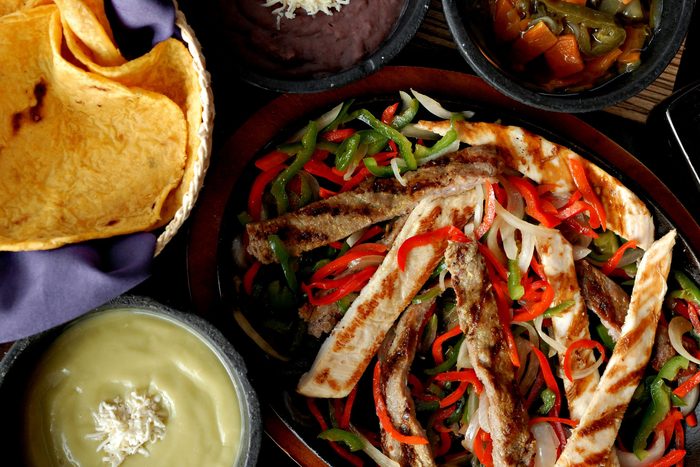 Chicken and beef fajitas with peppers and onions on an iron plate, with tortillas, beans and salsa