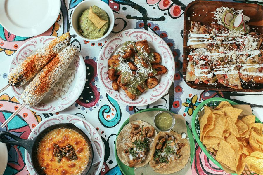 An overhead view of a Tex-Mex spread with tacos, elote, guacamole, chips and a skillet of melted cheese